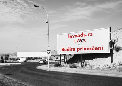 Crno bela fotografija velikog bilborda kraj puta sa crvenom reklamom za lavaads.rs - Budite primećeni.