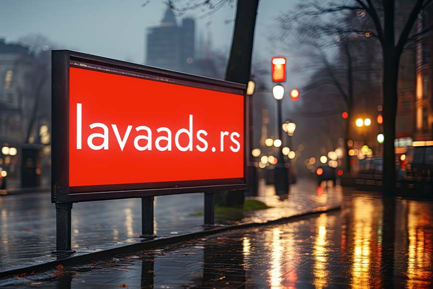 Iznajmljen bilbord sa natpisom lavaads.rs u fokusu, dok se u pozadini vidi ulica i grad u sumrak i mokri trotoar reflektuje svetla ulične rasvete nakon kiše.